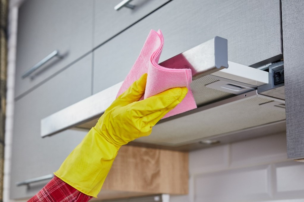 Persona Con Guante De Goma Amarillo Limpiando El Exterior De Una Campana De Cocina Con Un Paño Rosa